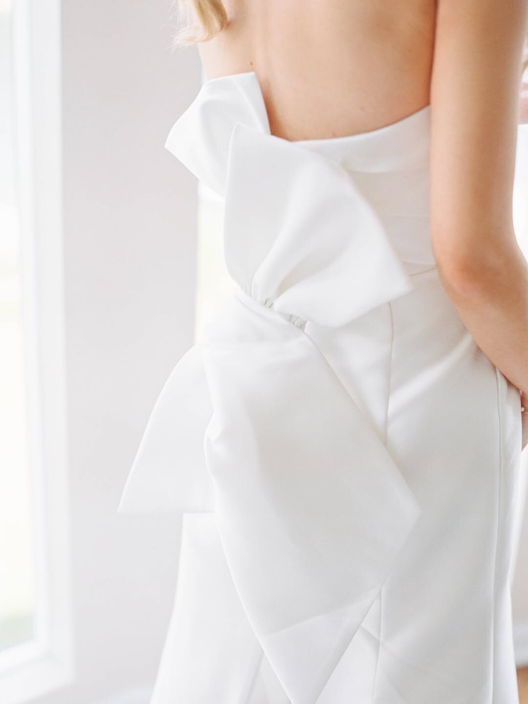 Wedding Photographer RI | Close-up of a woman in a white dress with a large bow on the back. The image conveys elegance and simplicity, with soft lighting and a serene mood.