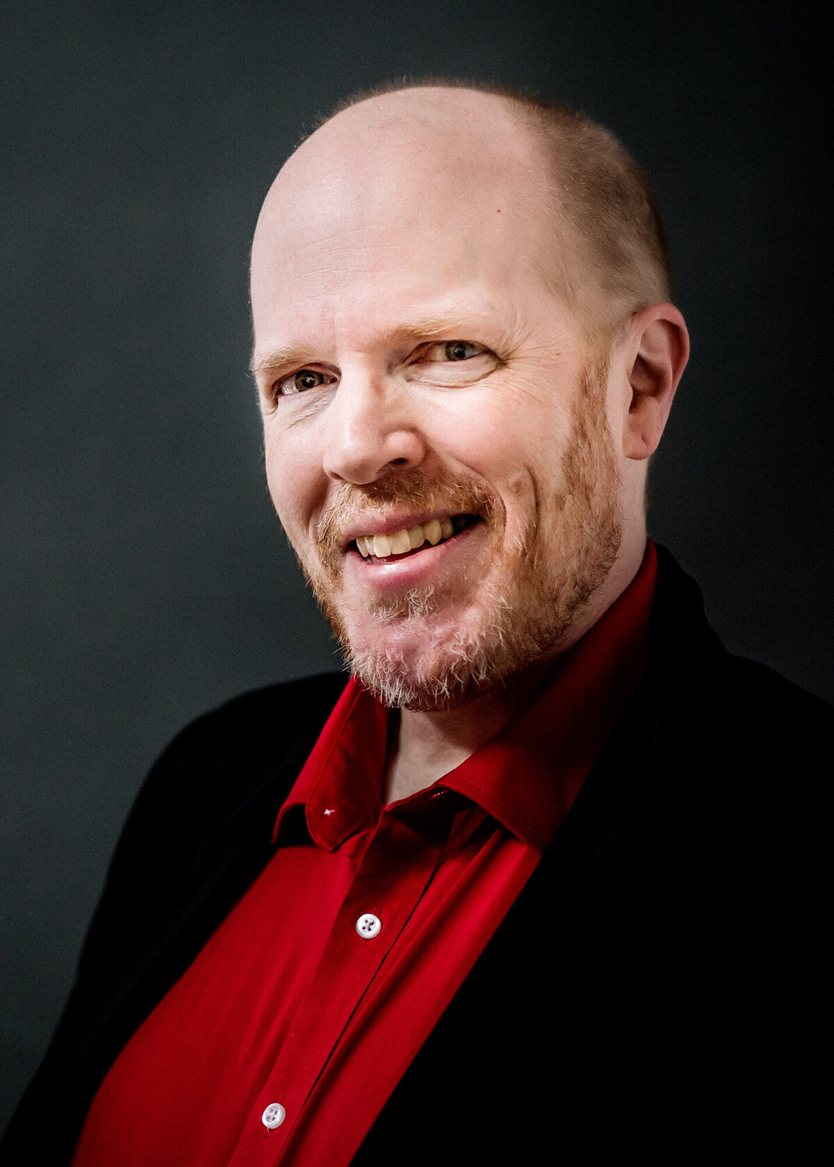 Male headshot client wearing a black suit & red shirt smiling at the camera