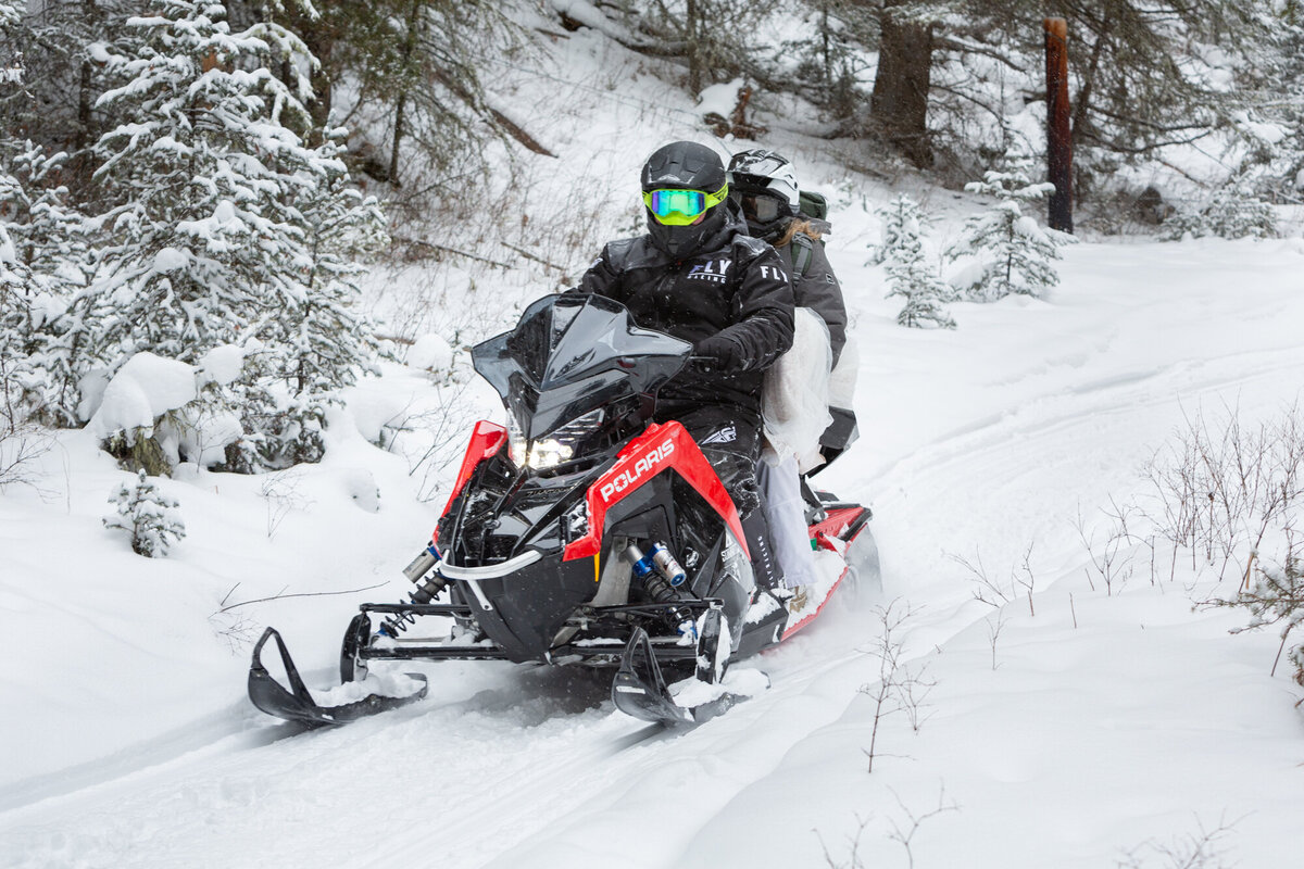 A bride and groom ride a snowmobile through the snow on their Montana elopement day.