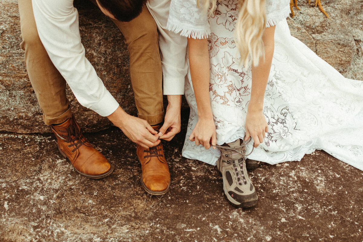 Bride and groom tying their laces on their boots before their hiking elopement