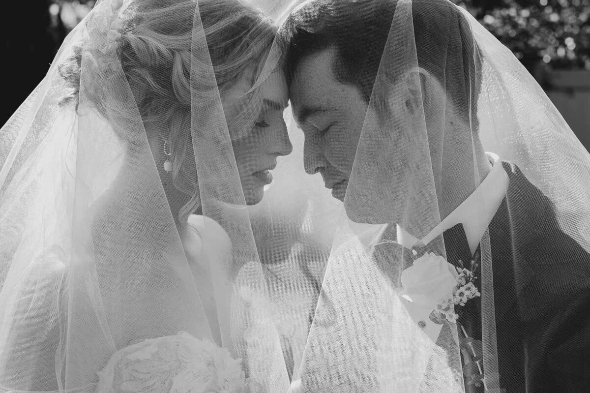 bride and groom touching foreheads under a veil