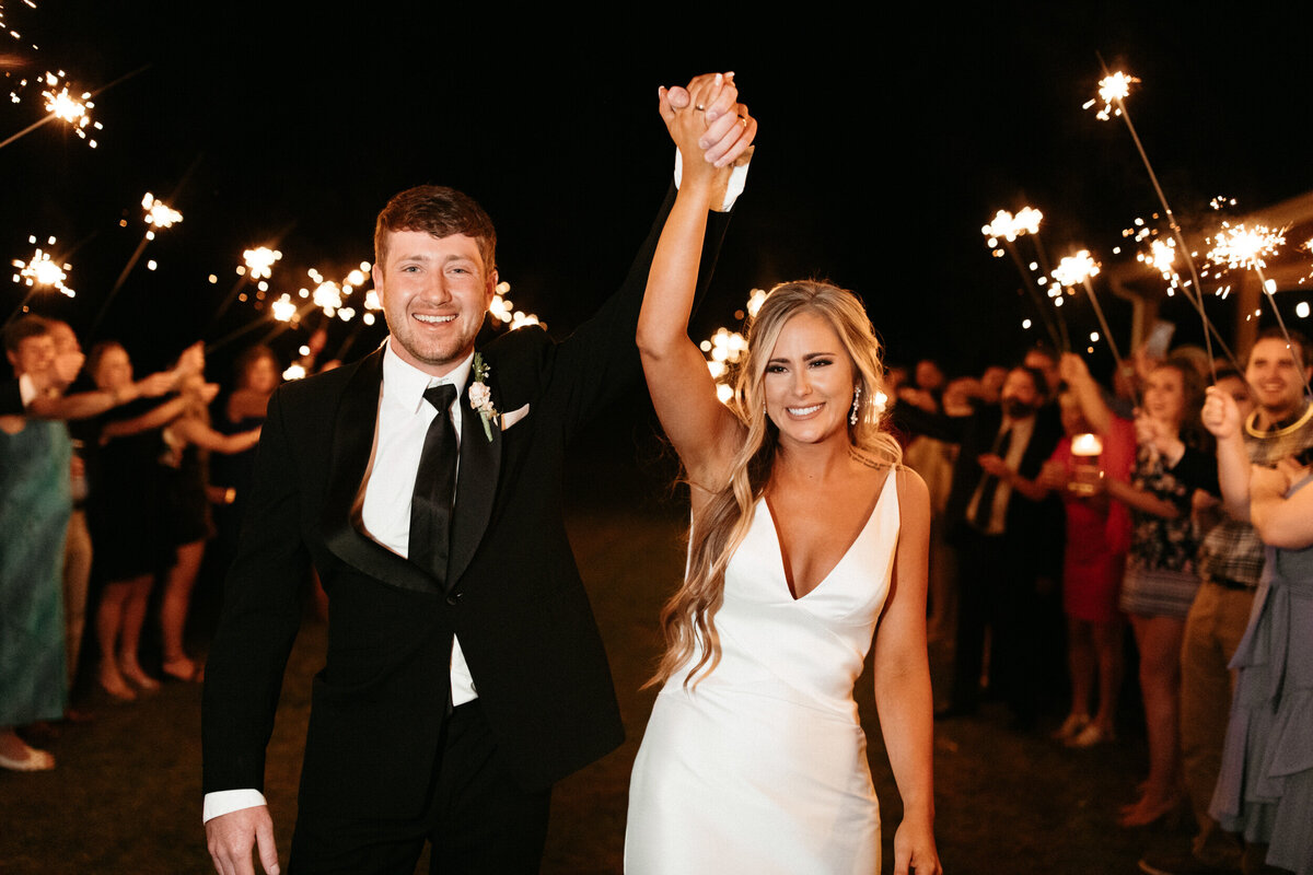 Bride and groom holding hands and running down the aisle of sparklers during their reception exit
