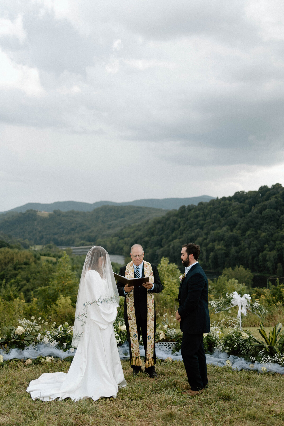Bride with a veil over her face during the wedding ceremony with mountains in the background.