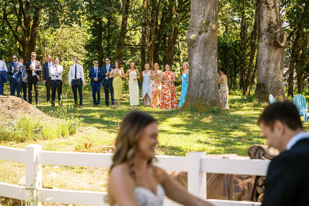 A group of people standing outdoors with the bride and groom out of focus in the foreground.