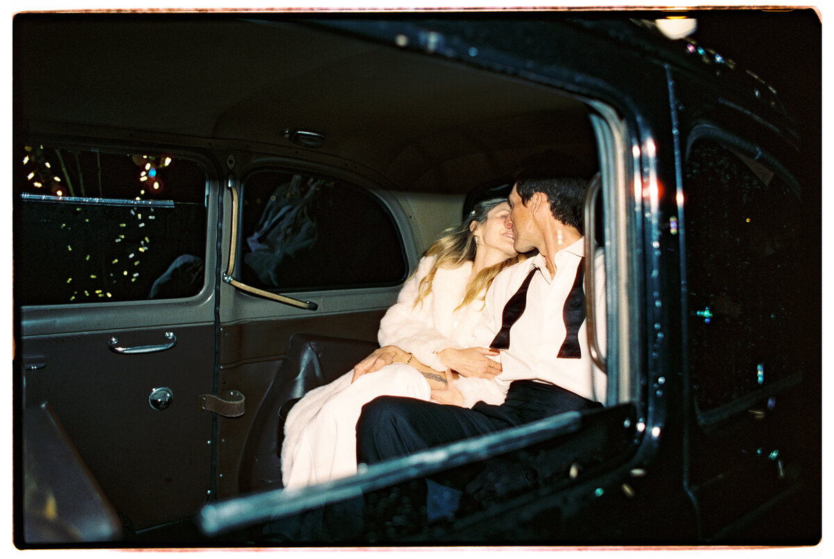 Couple kissing in a black cab, capturing a beautiful and meaningful send-off, photographed in a candid wedding photography style — Carmel wedding photography by Kate Winters Photography.