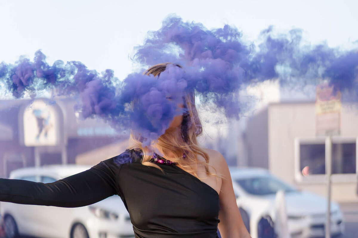 Entrepreneur holding purple smoke bomb outdoors, with vibrant smoke cloud swirling in front of her.