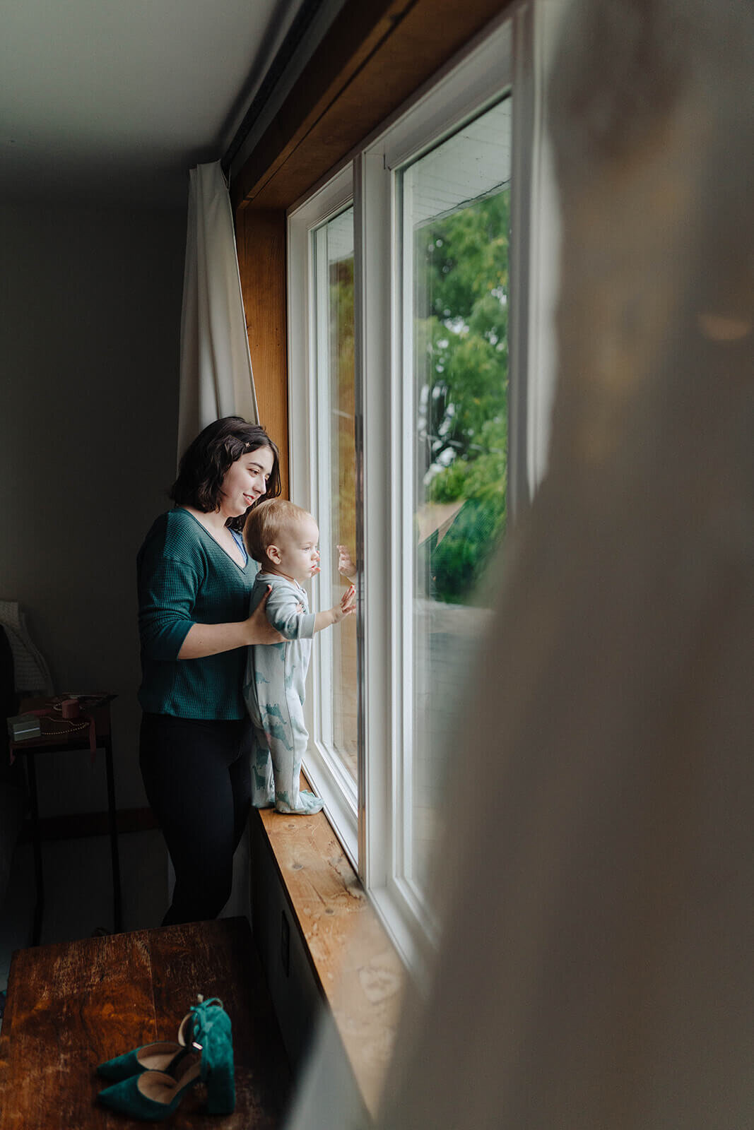 Woman holding baby on window sill looking out the window