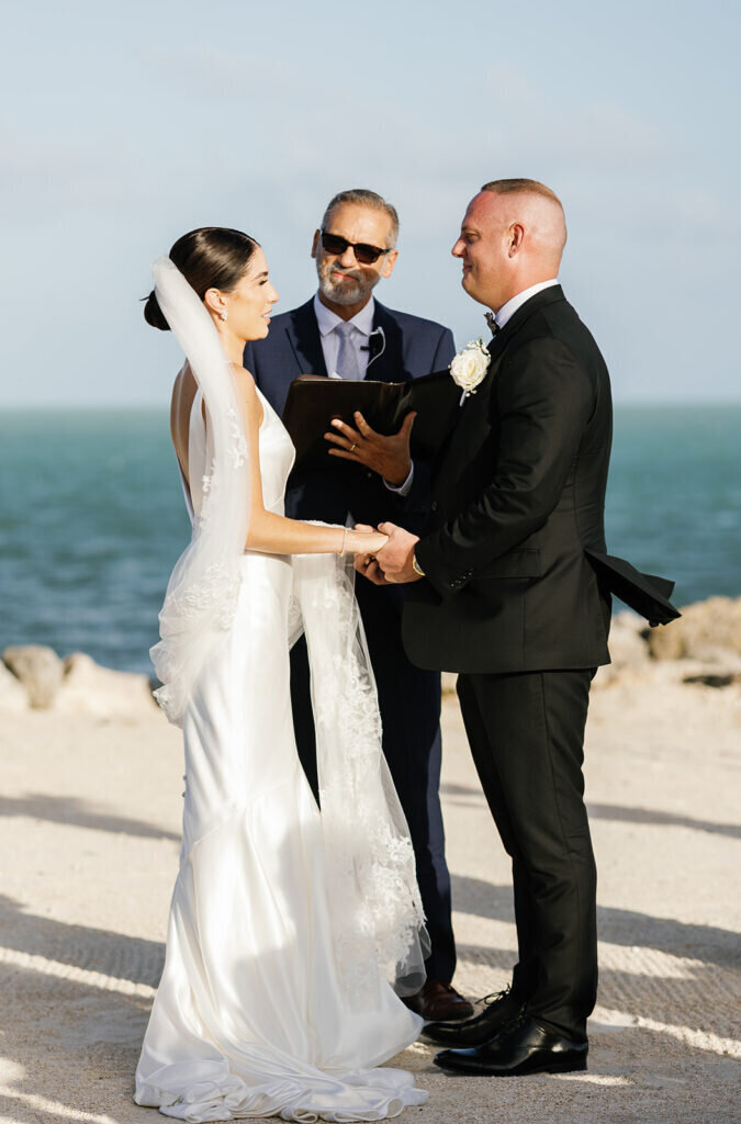 A romantic exchange of vows as the bride and groom hold hands with the ocean breeze in the background at their Florida Keys destination wedding. Captured by Claudia Amalia Photography.
