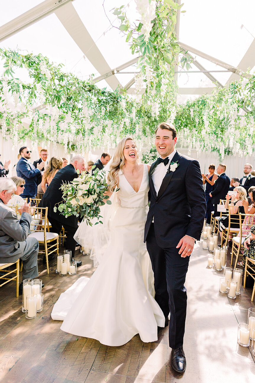 A beaming bride and groom walking down the aisle after saying "I do," surrounded by cheering guests and joyful celebration.