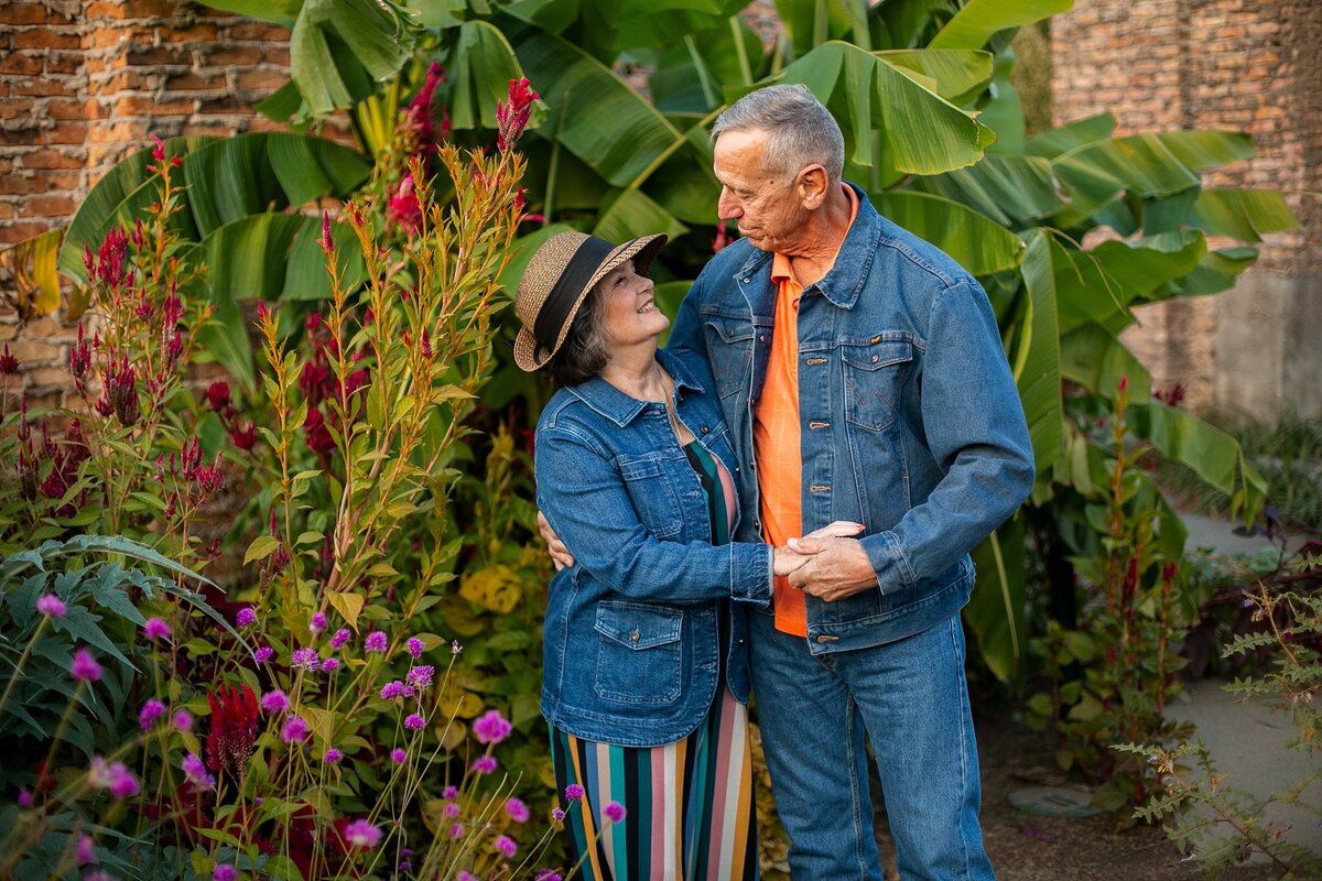 Senior-couple-holding-hands-smiling-at-each-other-in-a-lush-holliday-park-in-meridiankessler-meridian-kessler-wearing-denim-jackets-and-colorful-outfits