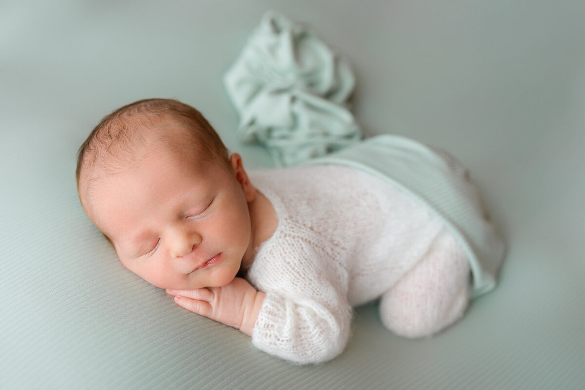 newborn boy posing on a sage green fabric with hand under chin in Savannah, Ga with Constance Calton Photography