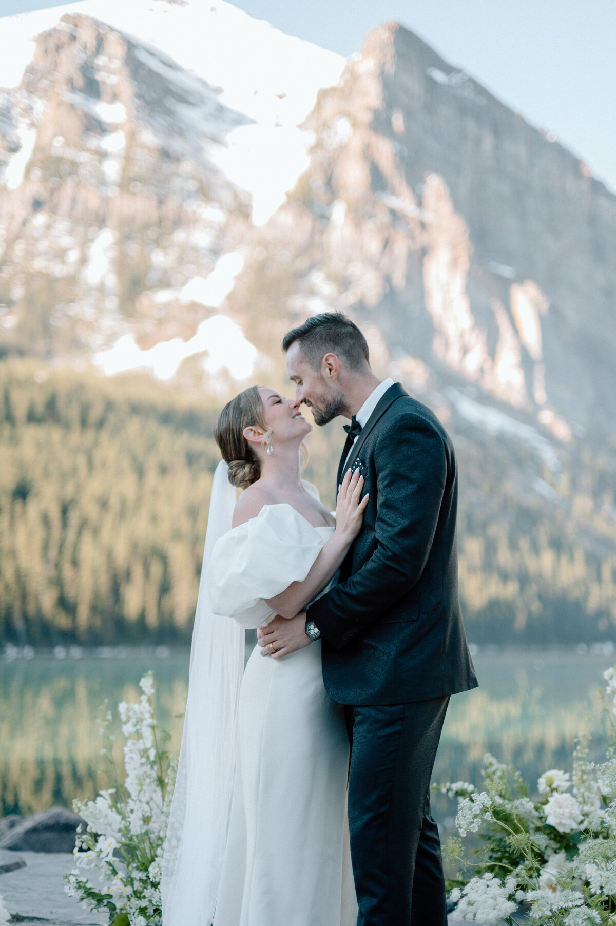 Groom kissing bride in front of snow-capped Lake Louise mountain view