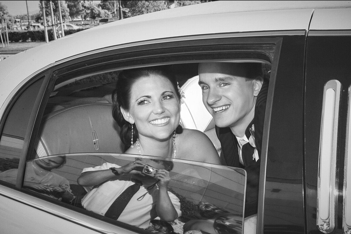 Bride and groom smile and look out car window of their vintage getaway car