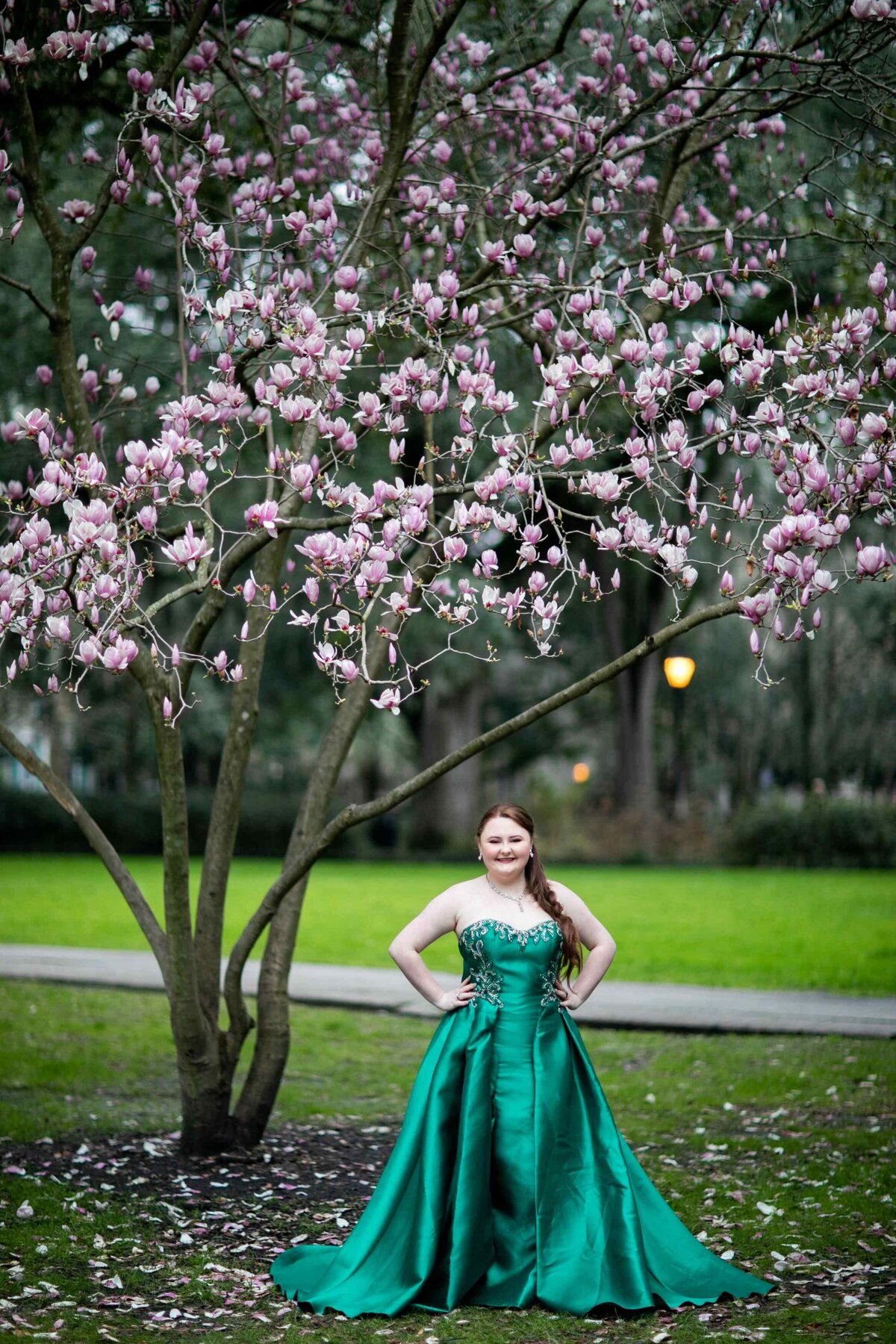 senior in green ballgown under tree with pink flowers