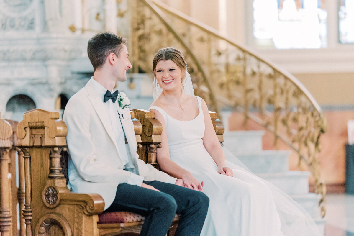 Bride and groom sitting while holding hands and smiling at once another during wedding Mass at Basilica St Josaphat in Milwaukee