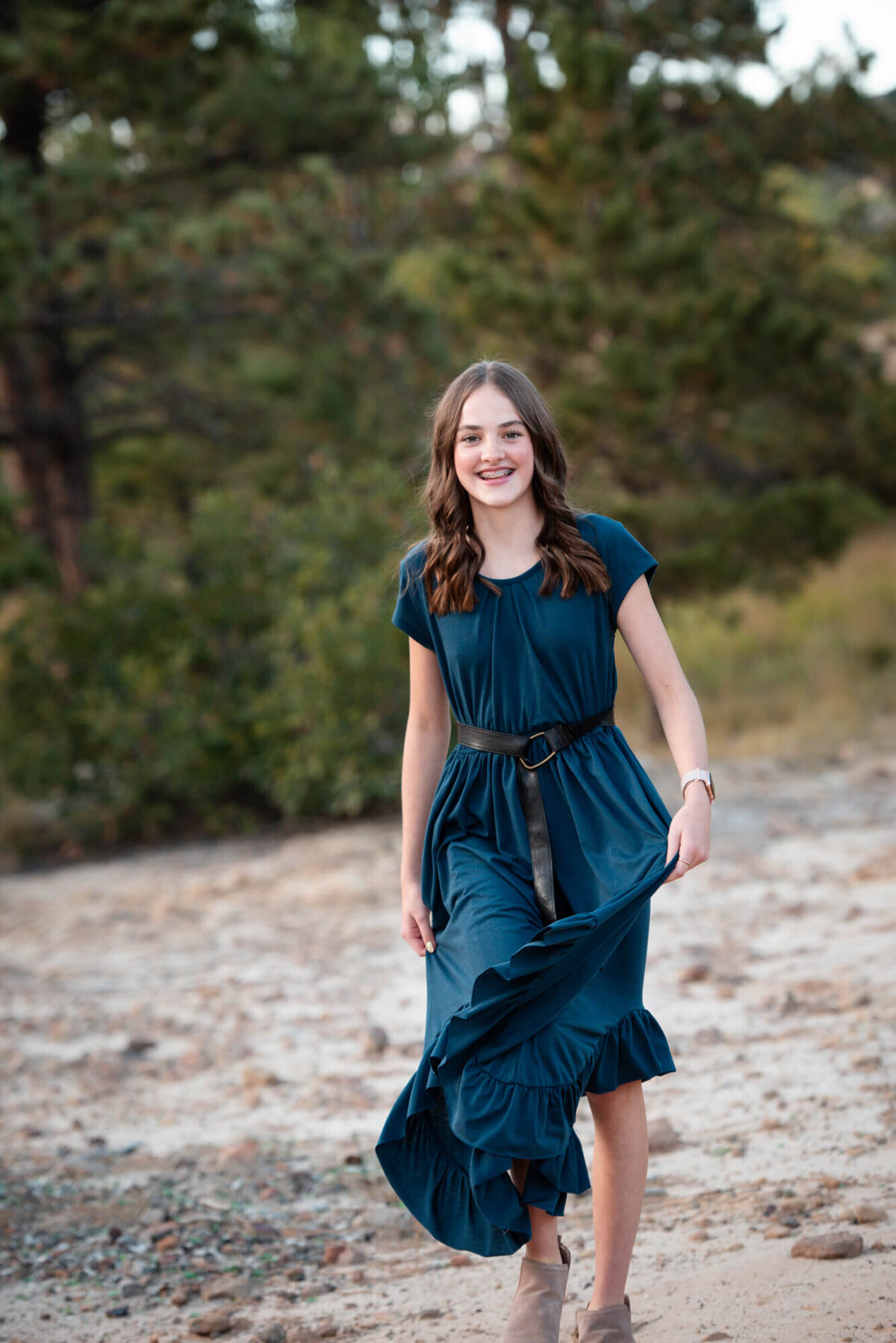 A teenage girl in a blue flowing dress walks up a trail smiling