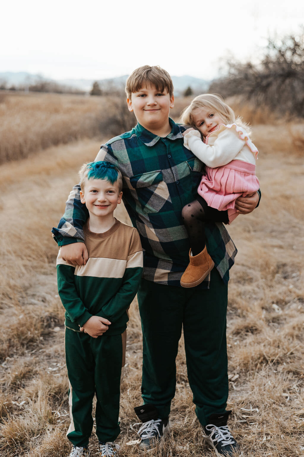 A child holding one sibling with one hand and resting their other hand on another sibling's shoulder.