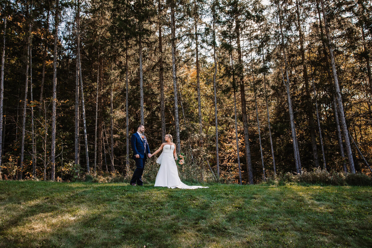 bride and groom hold hands on a hill in front of towering pine trees