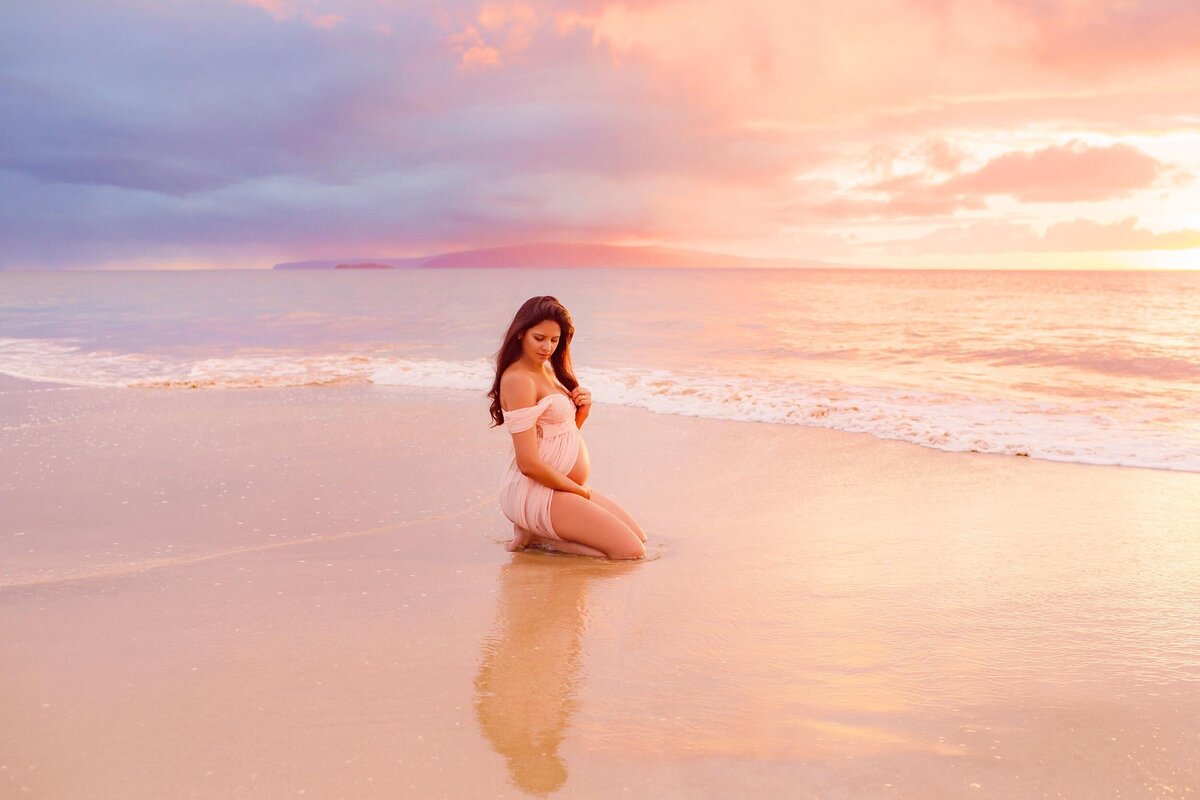 Woman kneeling on sand at sunset for maternity portraits on Maui