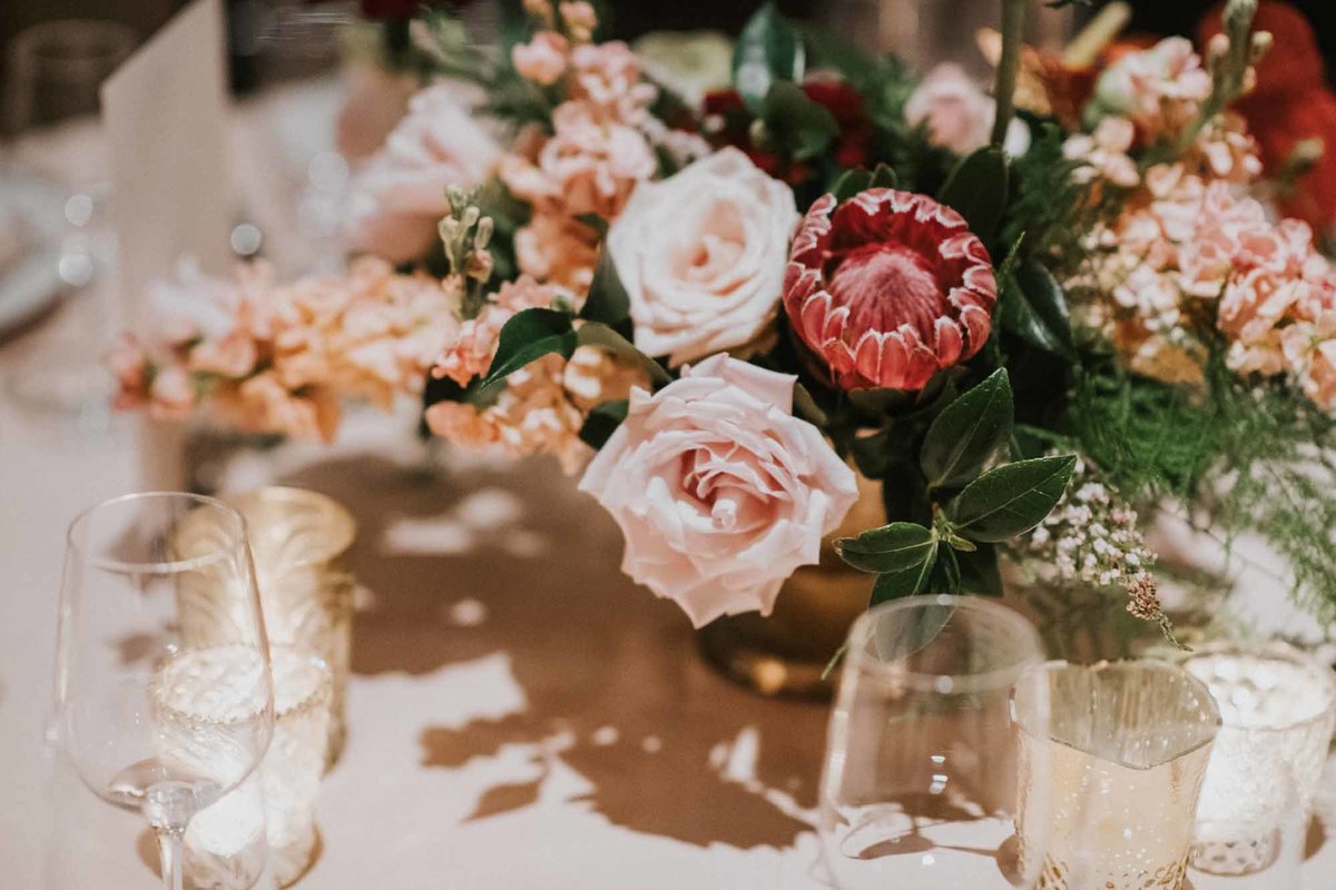 low centerpiece with pink protea, blush roses, peach stock, and greenery
