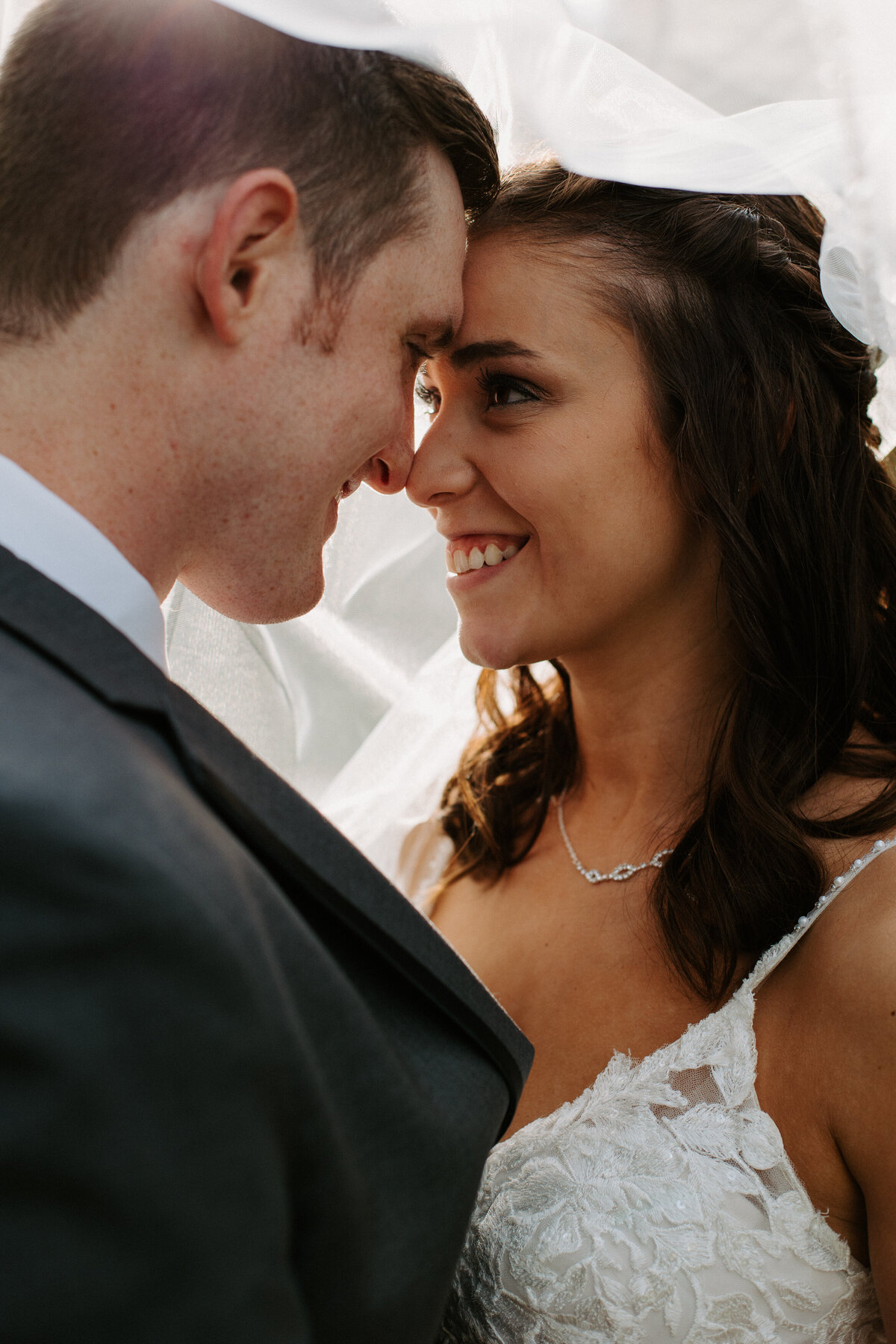 bride and groom smiling and touching foreheads as a veil drapes over them