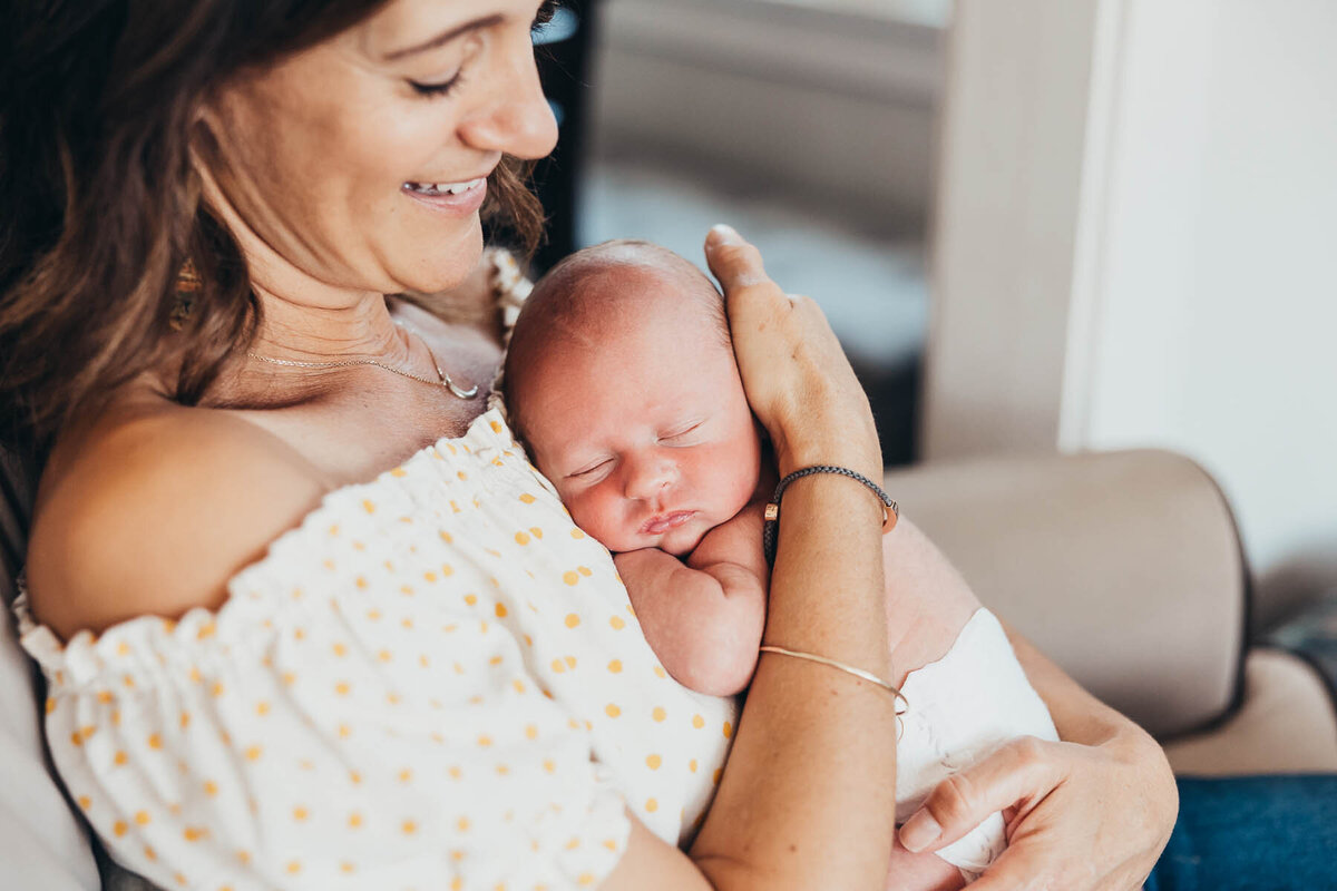 a beautiful mother holds her baby against her chest as he sleeps in their San Diego home