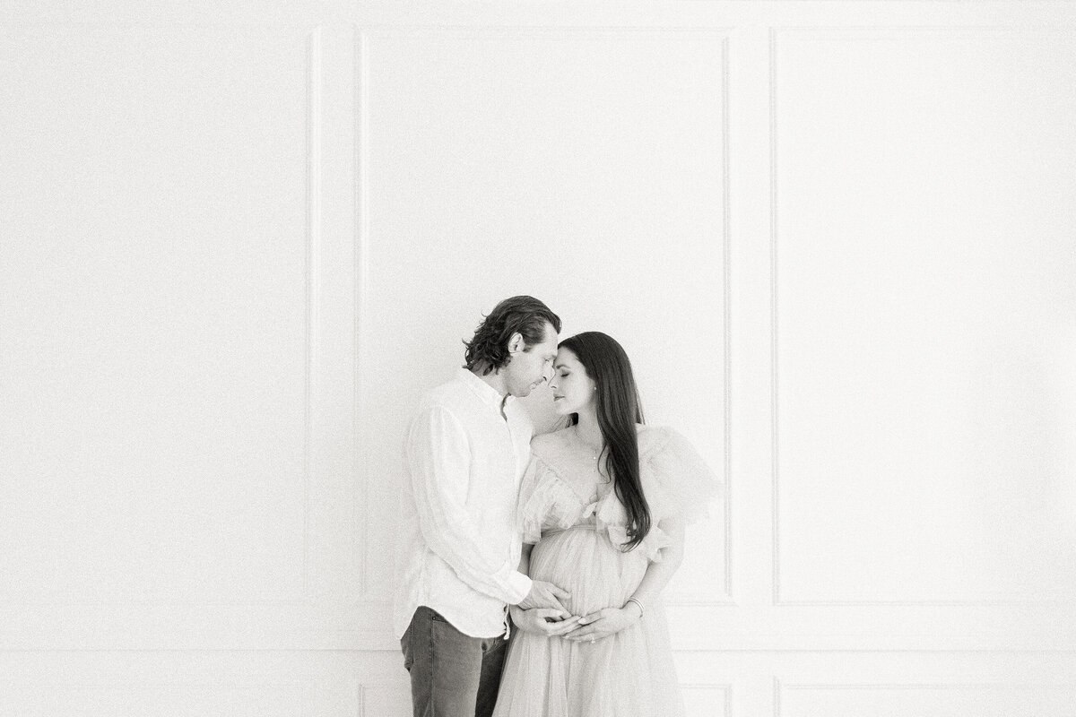 A beautiful black and white in studio maternity portrait of an expecting DFW mother being held by her spouse.