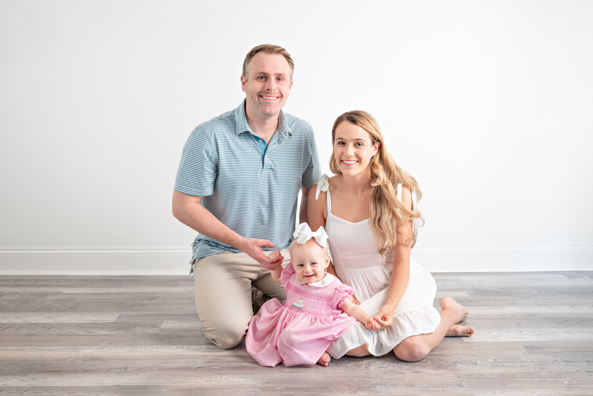 A mom and dad pose on the floor with their baby girl for family pictures in a studio in Huntsville Alabama