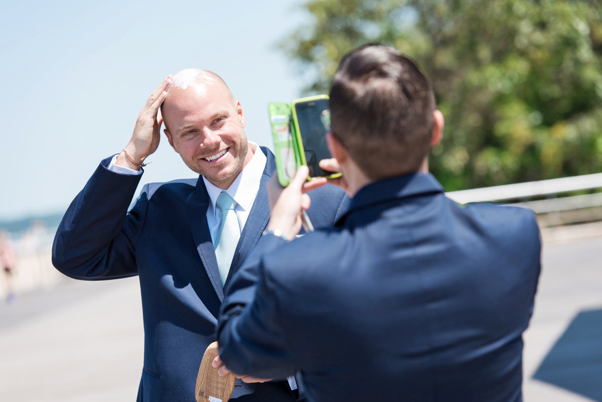 photo of groomsmen taking a photo of groom smiling on the beach from wedding at Pavilion at Sunken Meadow