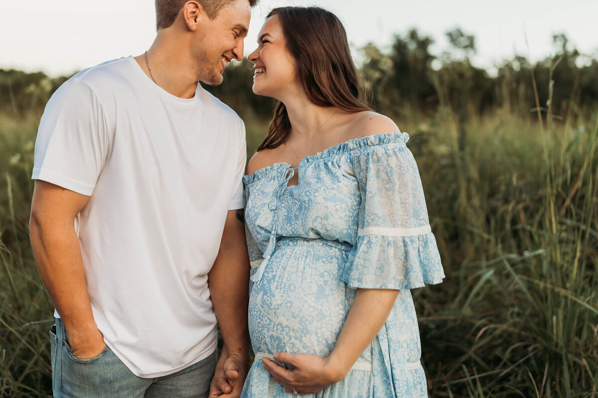 woman leans in for a kiss while holding hands with dad and caressing her belly.