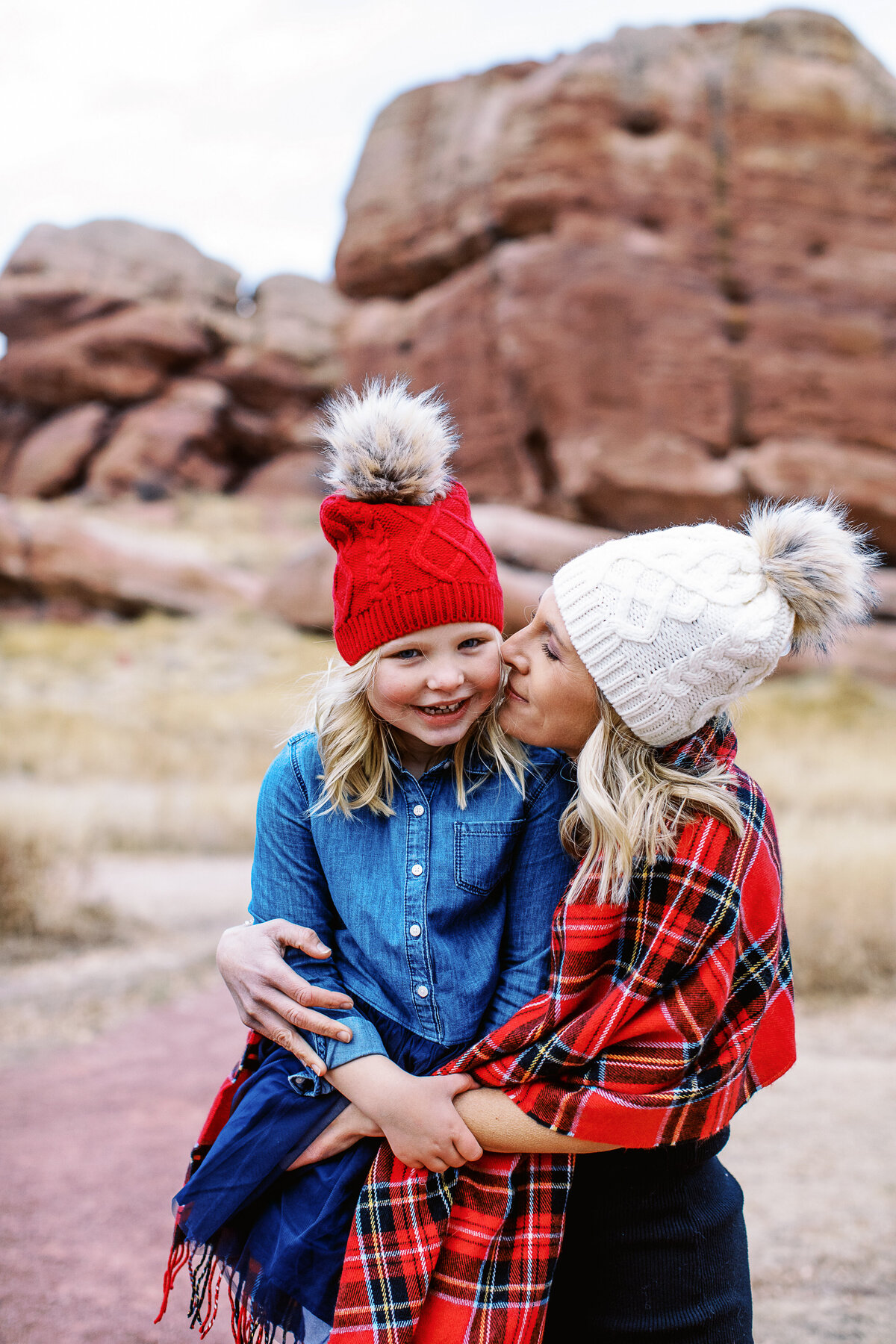 a mom in red plaid scarf looks at daughter who wears red beanie