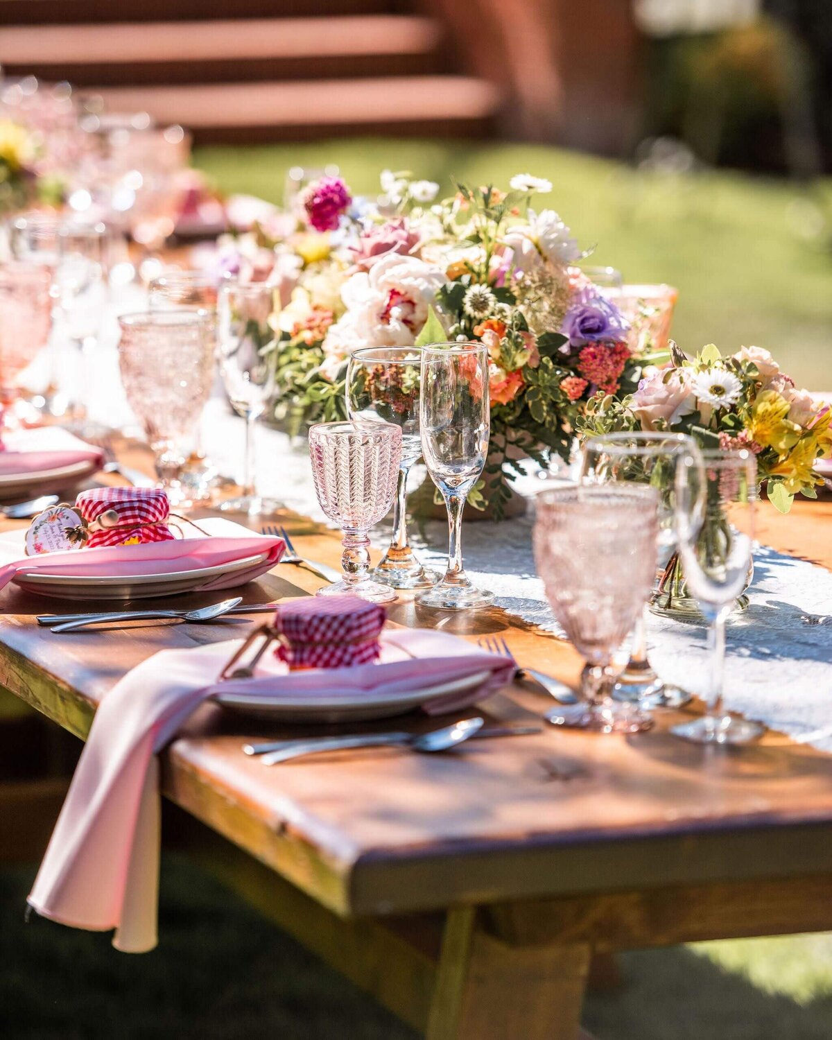 Outdoor wedding reception table featuring place settings and large floral arrangement.