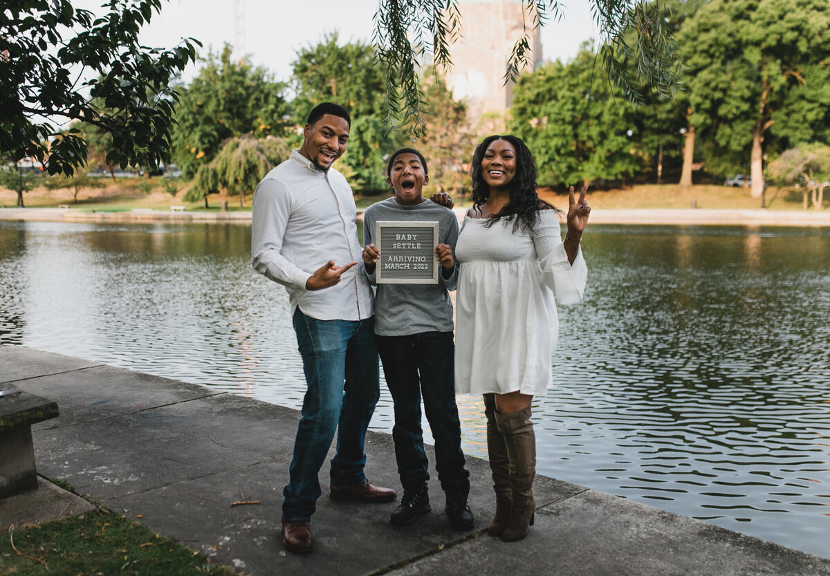 Pregnancy announcement photoshoot with a mom, dad, and child standing outside.