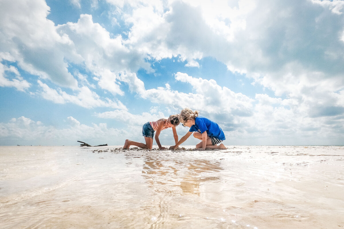 Brother and sister are playing on the beach in shallow water.
