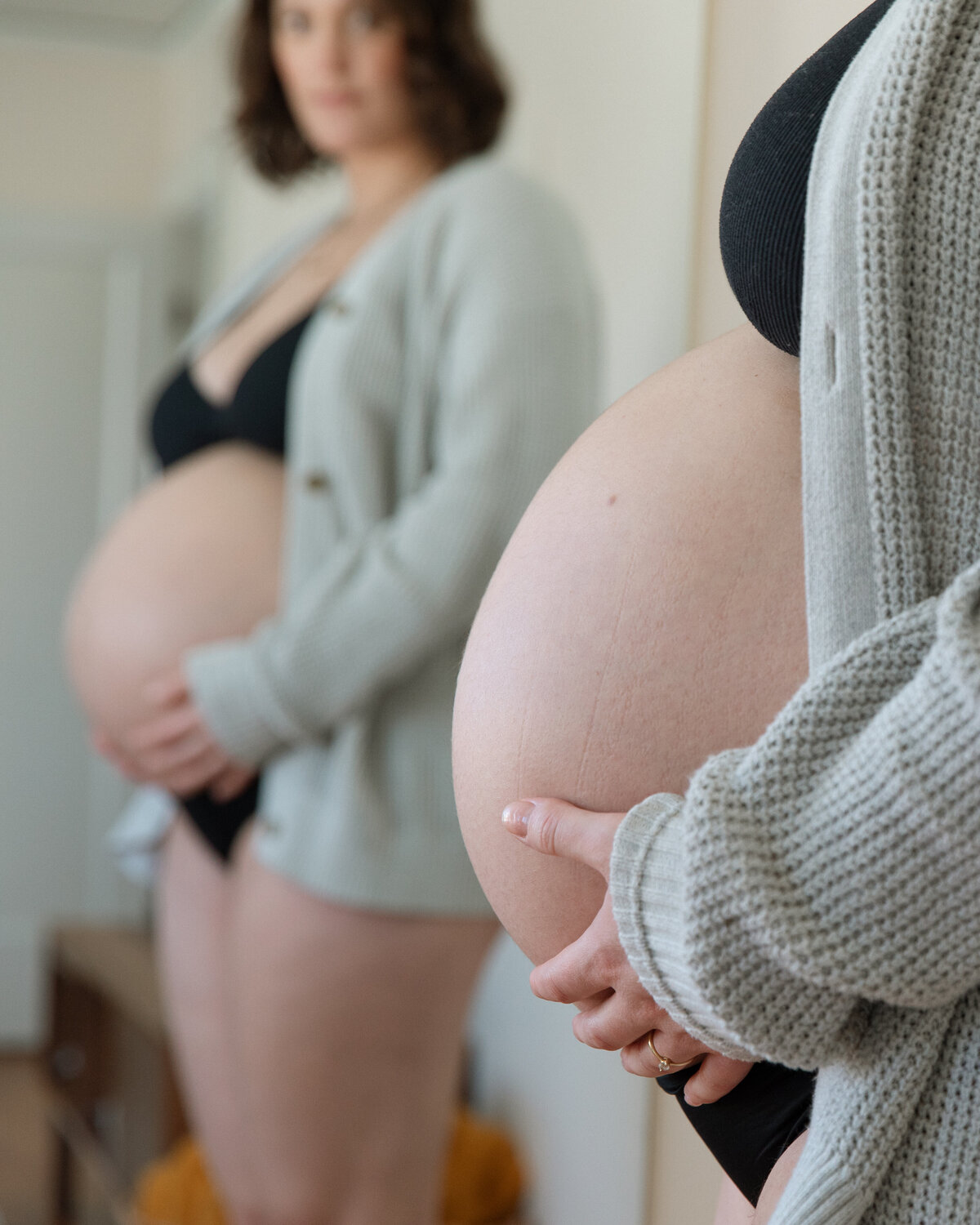 pregnant woman standing in front of a mirror, gently looking at her belly.