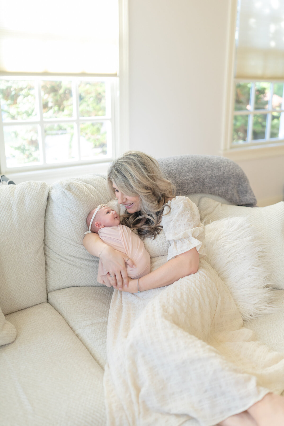 Lifestyle in-home newborn session featuring a mother relaxing on the couch, laying next to her newborn. She gazes lovingly at her baby, capturing a tender and intimate moment in a cozy home setting