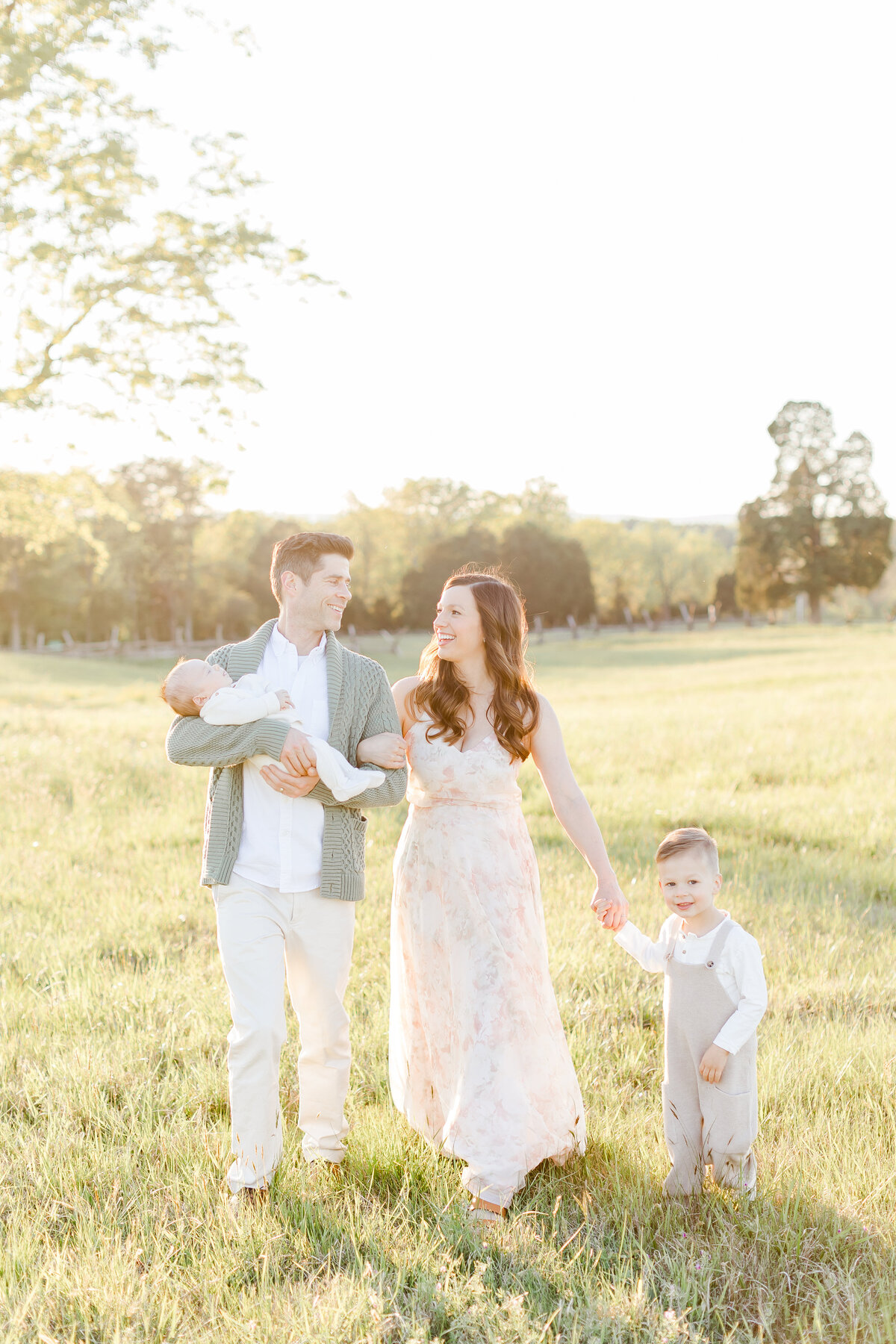 A family walking holding hands outside in a field at a Northern Virginia Newborn Photography session