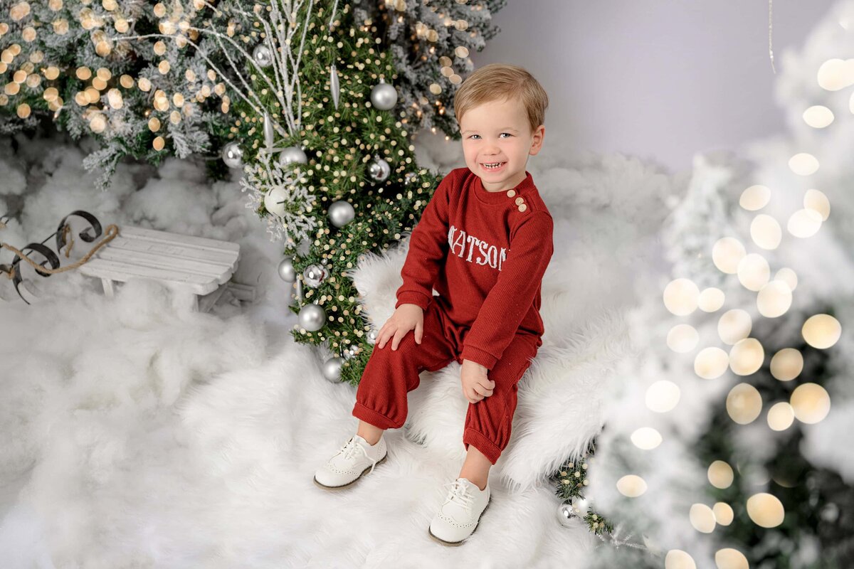 little boy dressed in red smiles in white christmas set