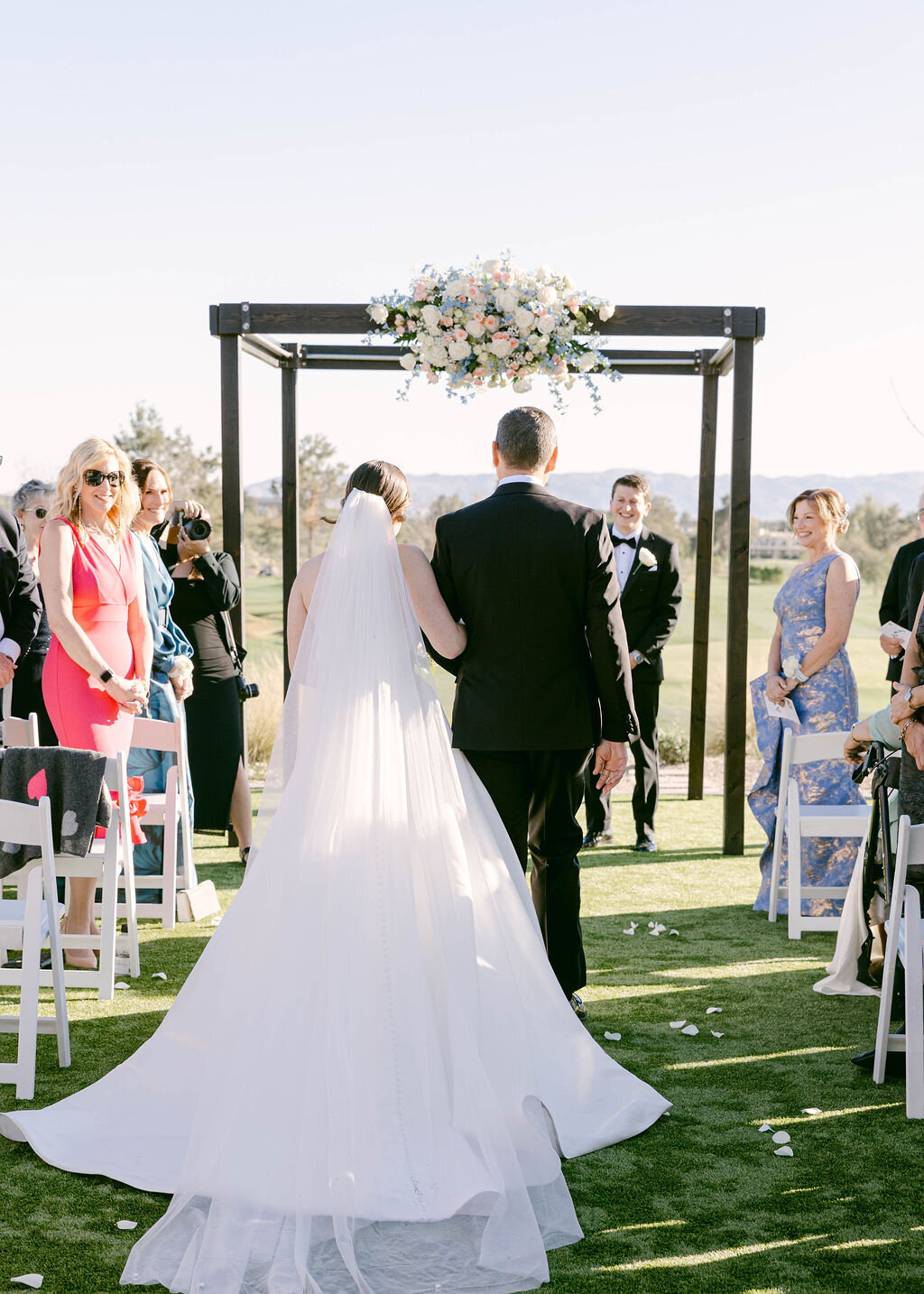 Bride and father walking down aisle toward groom at Arizona Biltmore outdoor ceremony.