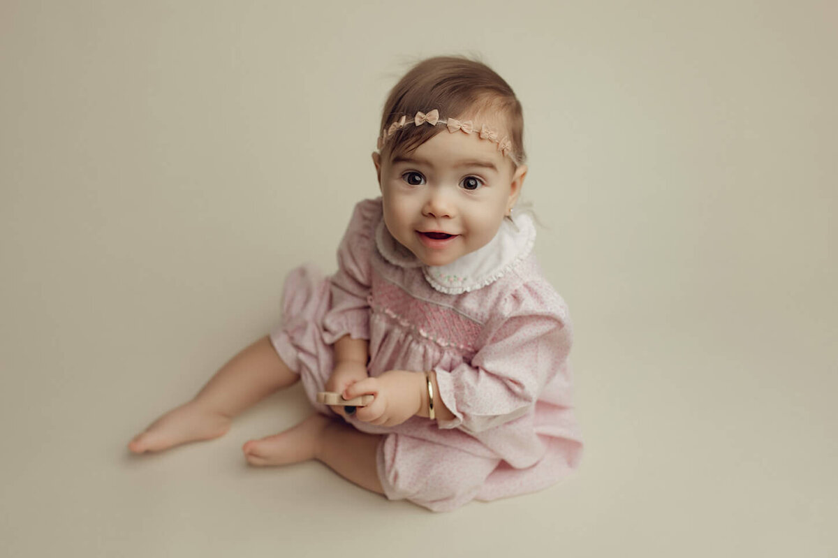 a one year old girl wearing a vintage pink outfit sitting and smiling