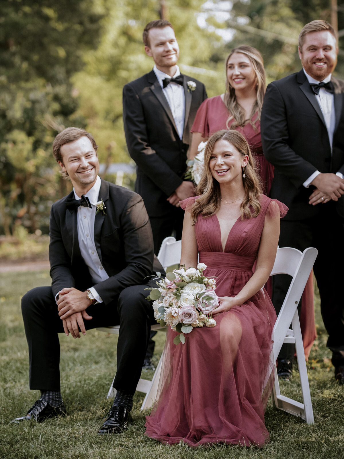 candid-photo-of-jovial-bridal-party-sitting-on-lawn-in-white-chairs