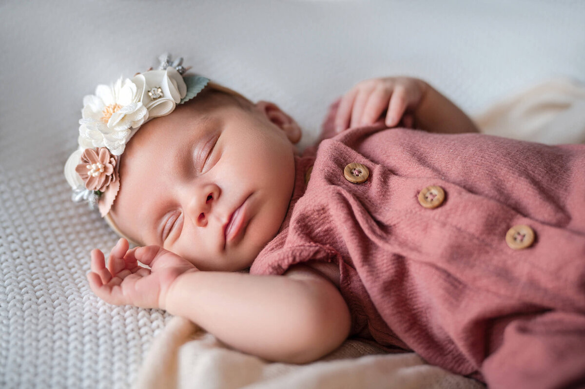 newborn girl with pink onesie and floral headband sleeping