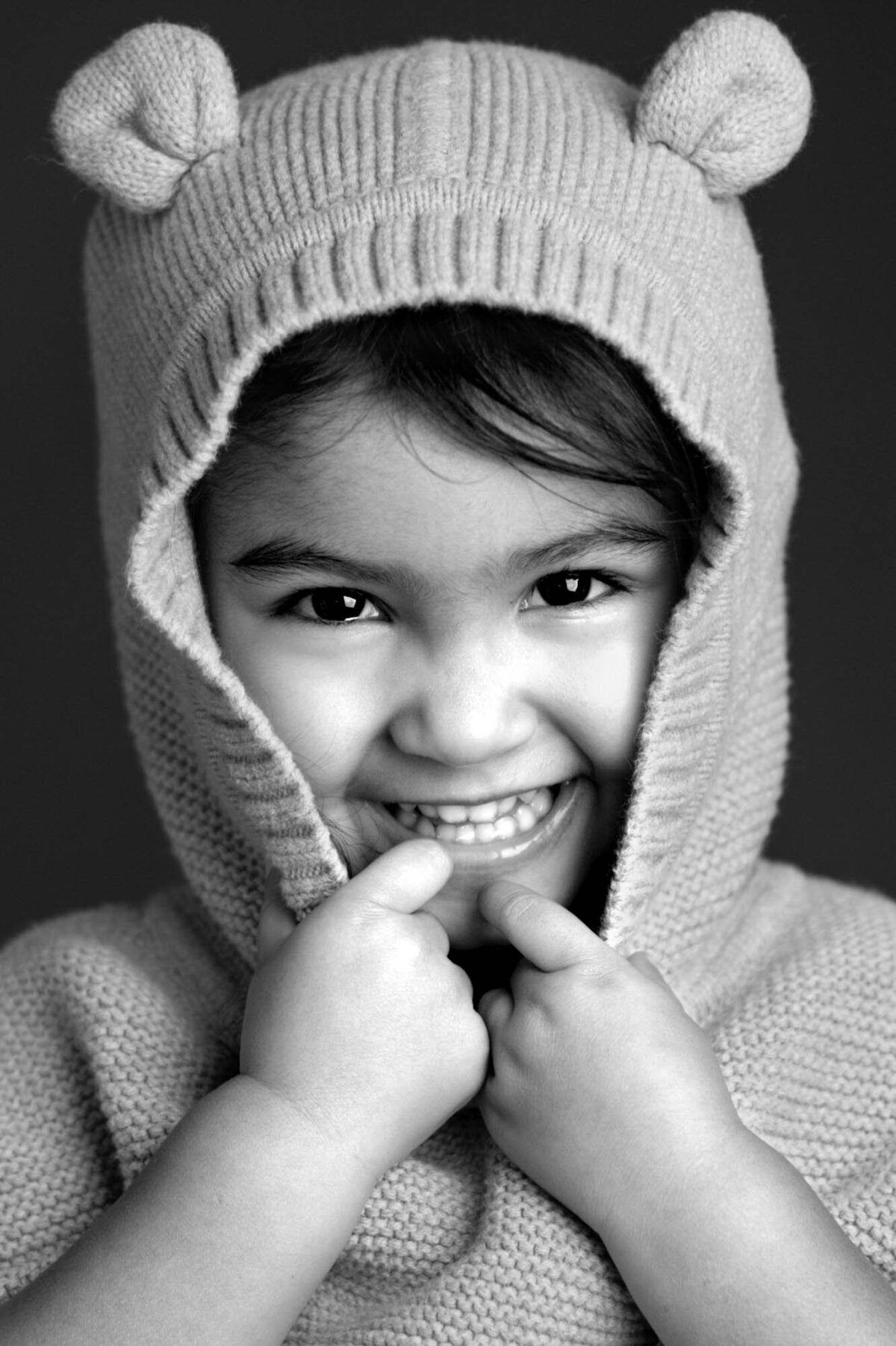 A little girl smiles while wearing a cozy knitted bear hoodie with ears, adding a playful touch to her outfit.