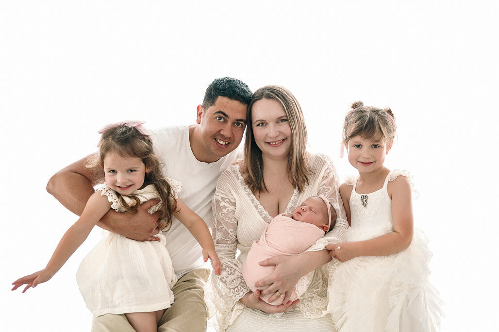 family of 5 enjoying their newborn baby girl in white studio setting