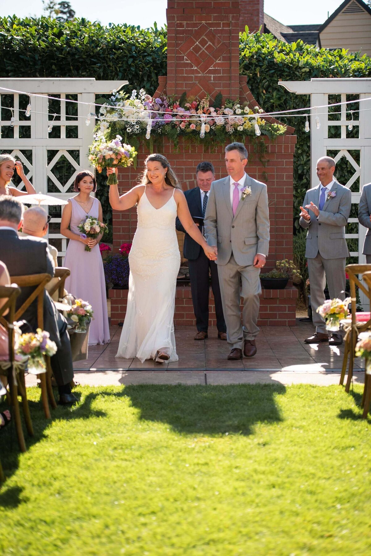 Bride and groom smile and she holds a bouquet as they walk up the aisle.