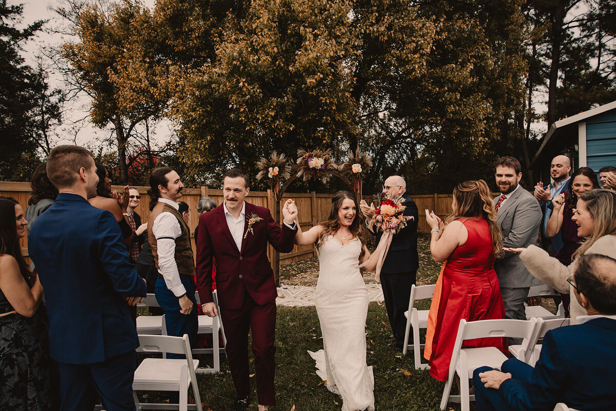 A couple holding hands and celebrating as they walk back up the aisle after their wedding 