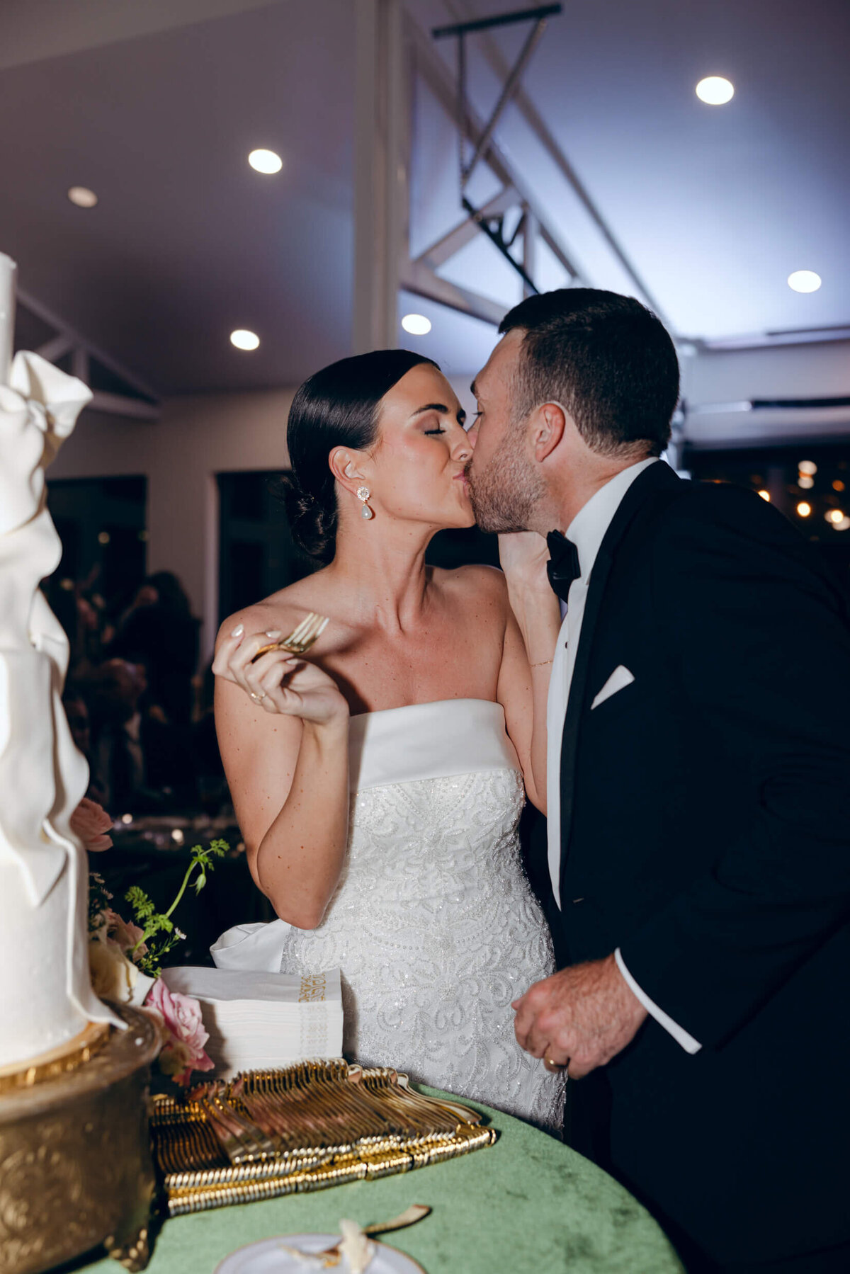 A candid wedding photo of the bride and groom and kissing after eating a piece of their wedding cake