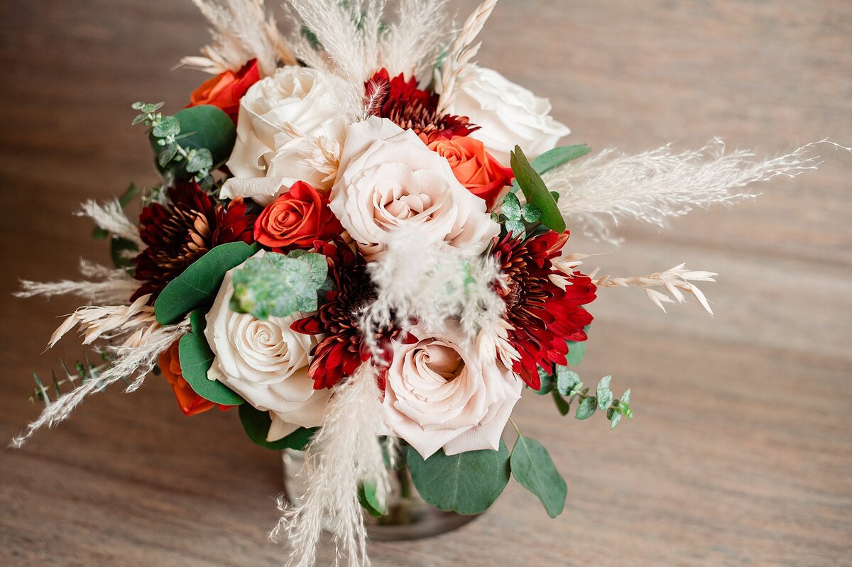 A circular bridal bouquet with blush roses, orange tea roses and crimson dahlias accented with silver dollar eucalyptus and pampas grass.