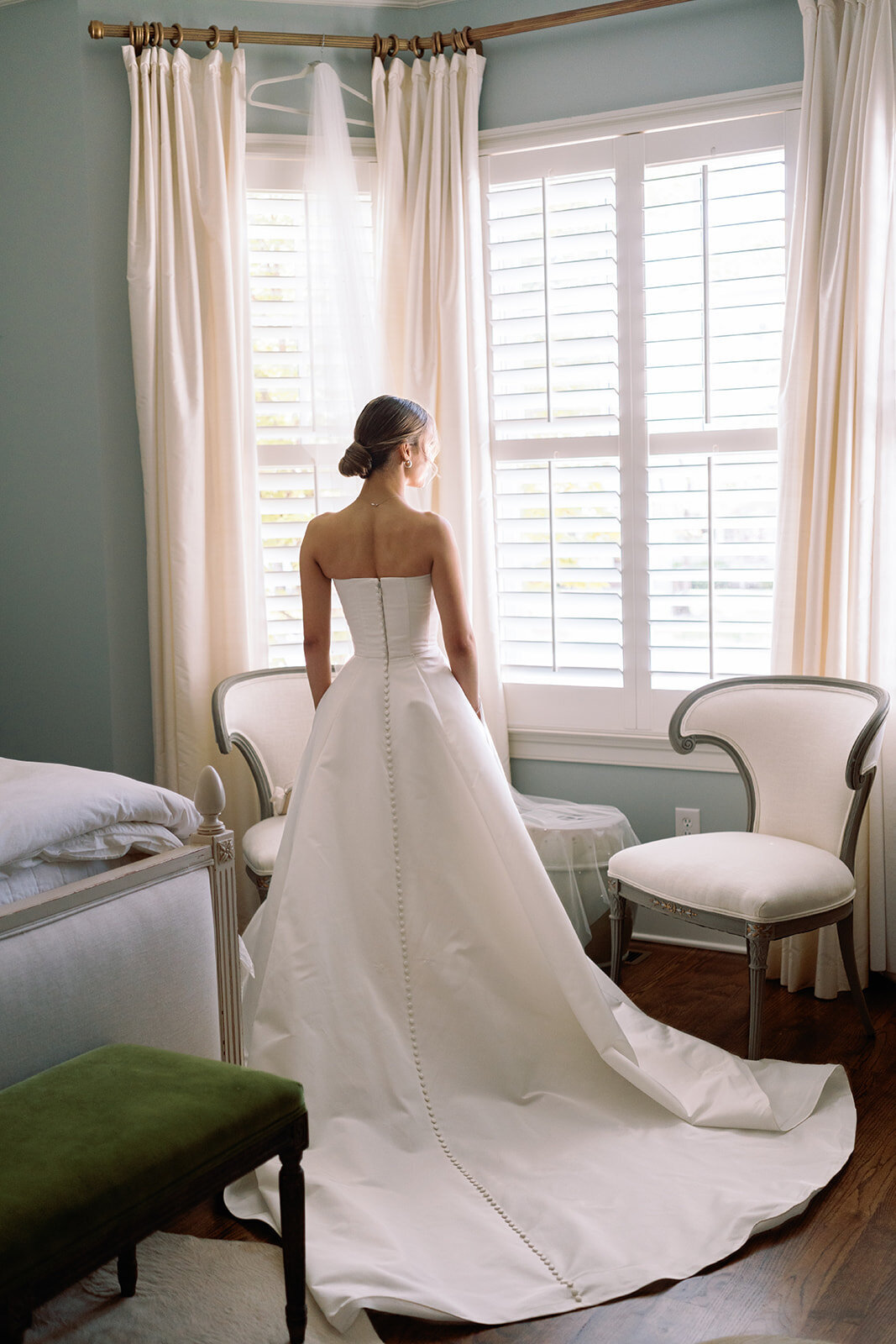 Bride standing in front of a sunlit window in her strapless wedding gown, looking outside before the ceremony at Burritt on the Mountain in Huntsville, Alabama, photographed by Perry Hancock.
