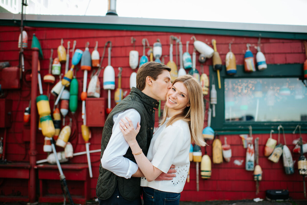 boston engaged couple kissing in seaport district in front of buoys